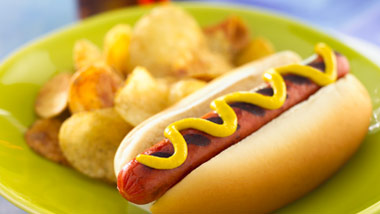 hot dog with mustard and chips on a lime green plate