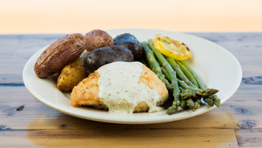 plate of chicken, potatoes and asparagus on a wooden background
